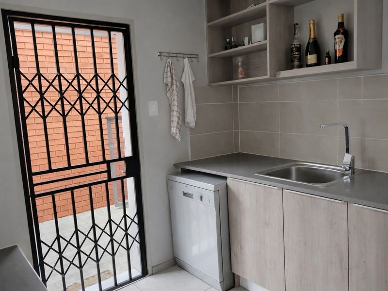 A functional scullery area featuring built-in cabinetry, open shelving, a stainless steel sink with mixer tap, and a secure exterior access door.