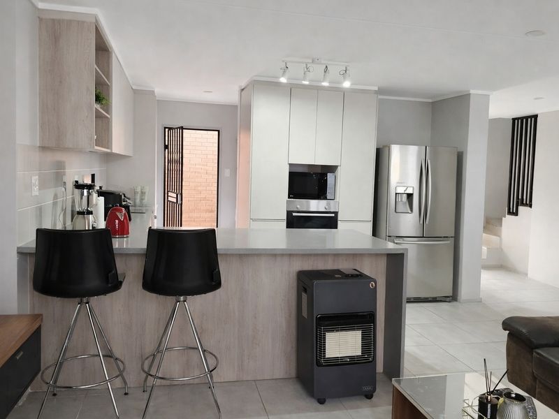 Modern open-plan kitchen featuring sleek cabinetry, stone countertops, and integrated appliances, seamlessly flowing into the living area with tiled flooring throughout.