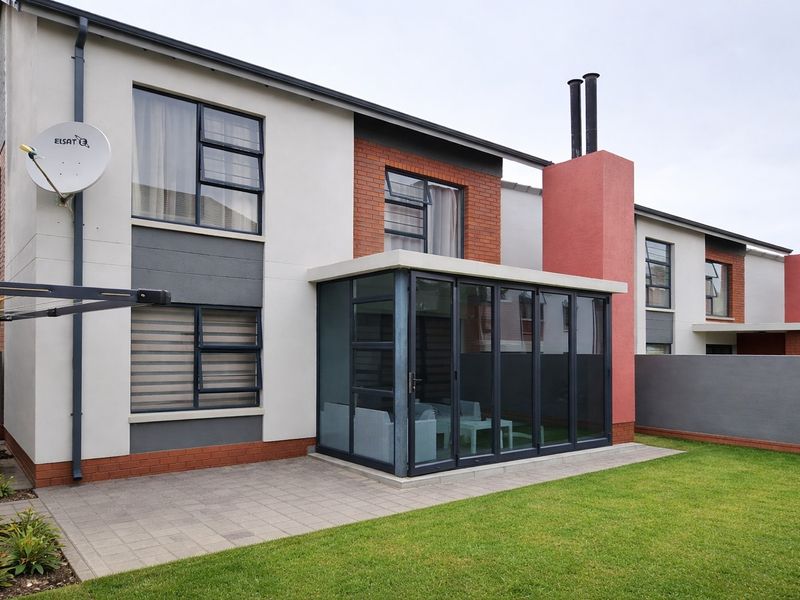Rear view of the townhouse featuring a paved patio, an enclosed sunroom with aluminium frames, a brick chimney, and a well-maintained garden.