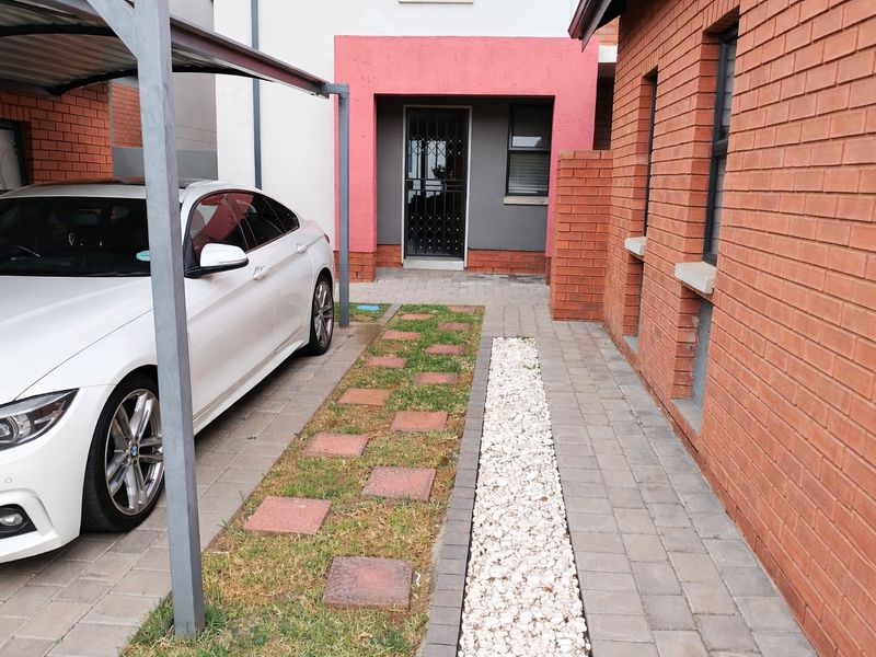 Front exterior view of the townhouse featuring a covered carport, paved driveway, and a secure entrance with a metal security gate.