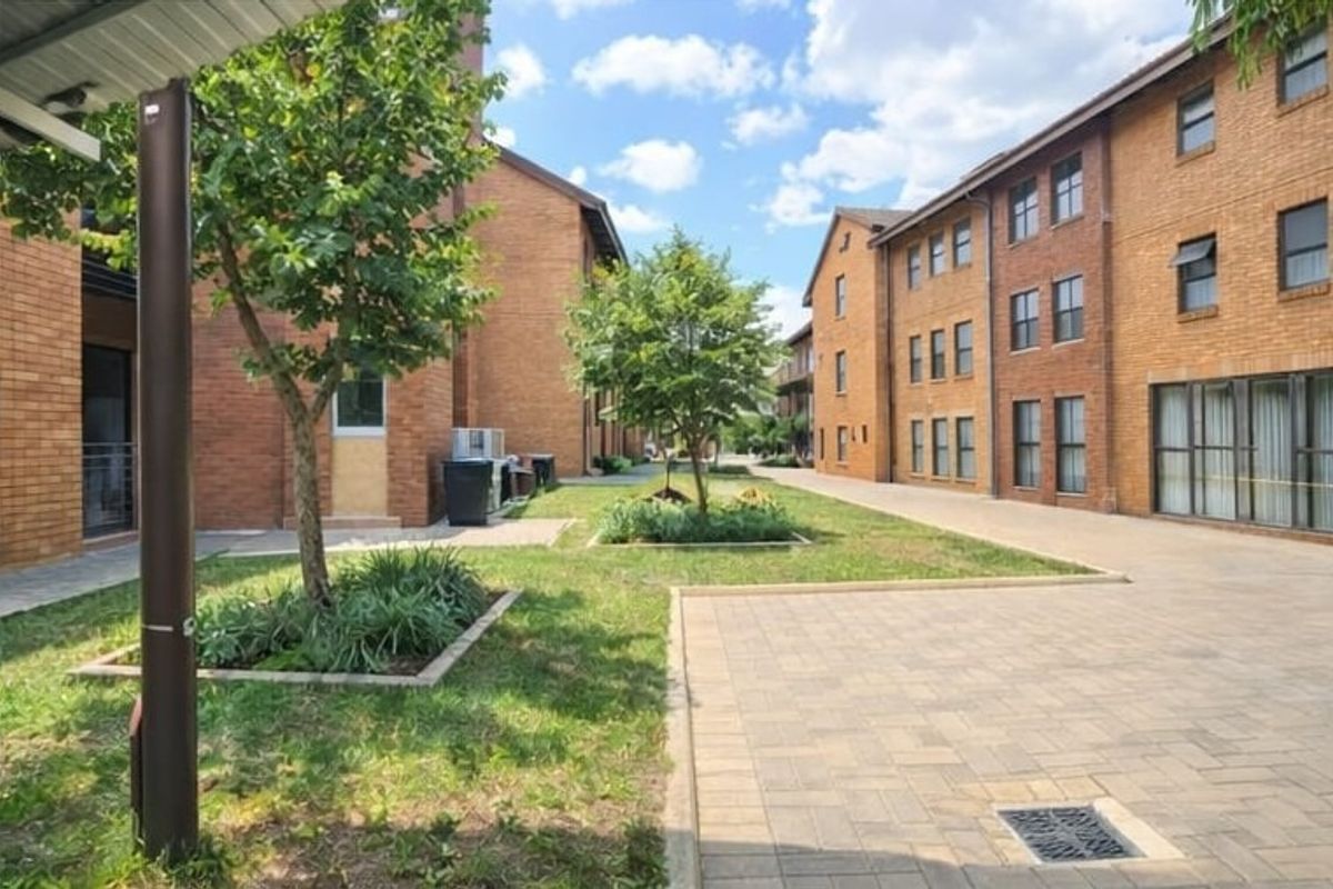 A view of the communal courtyard area between brick apartment buildings, featuring paved walkways and landscaped garden beds.