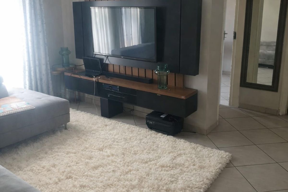 A well-maintained living room featuring a modern built-in media unit and neutral tiled flooring, providing a functional and comfortable living space.