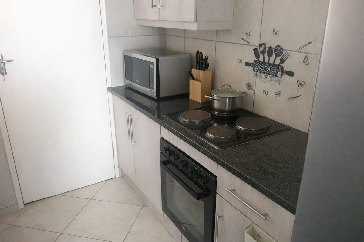 Compact kitchen featuring modern light-toned cabinetry, dark granite countertops, a built-in electric oven and hob, and neutral tiled flooring.