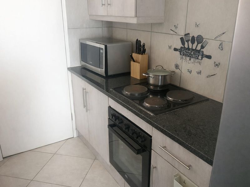 Compact kitchen featuring modern light-toned cabinetry, dark granite countertops, a built-in electric oven and hob, and neutral tiled flooring.