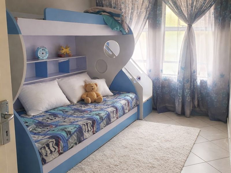 A bedroom featuring tiled flooring and large windows with curtain rails, providing natural light to the space.