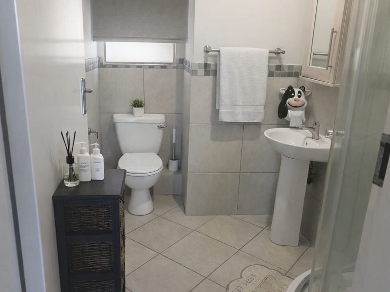 A functional bathroom featuring a pedestal basin, toilet, and shower enclosure with neutral wall and floor tiling.
