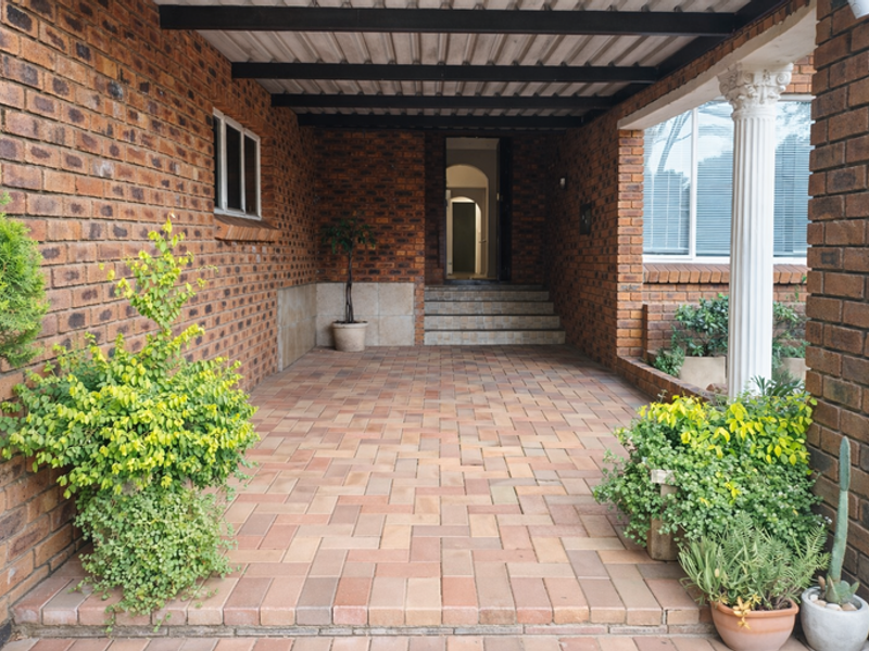 A covered patio entrance featuring brick walls, paved flooring, and a decorative column leading to the main house entrance.