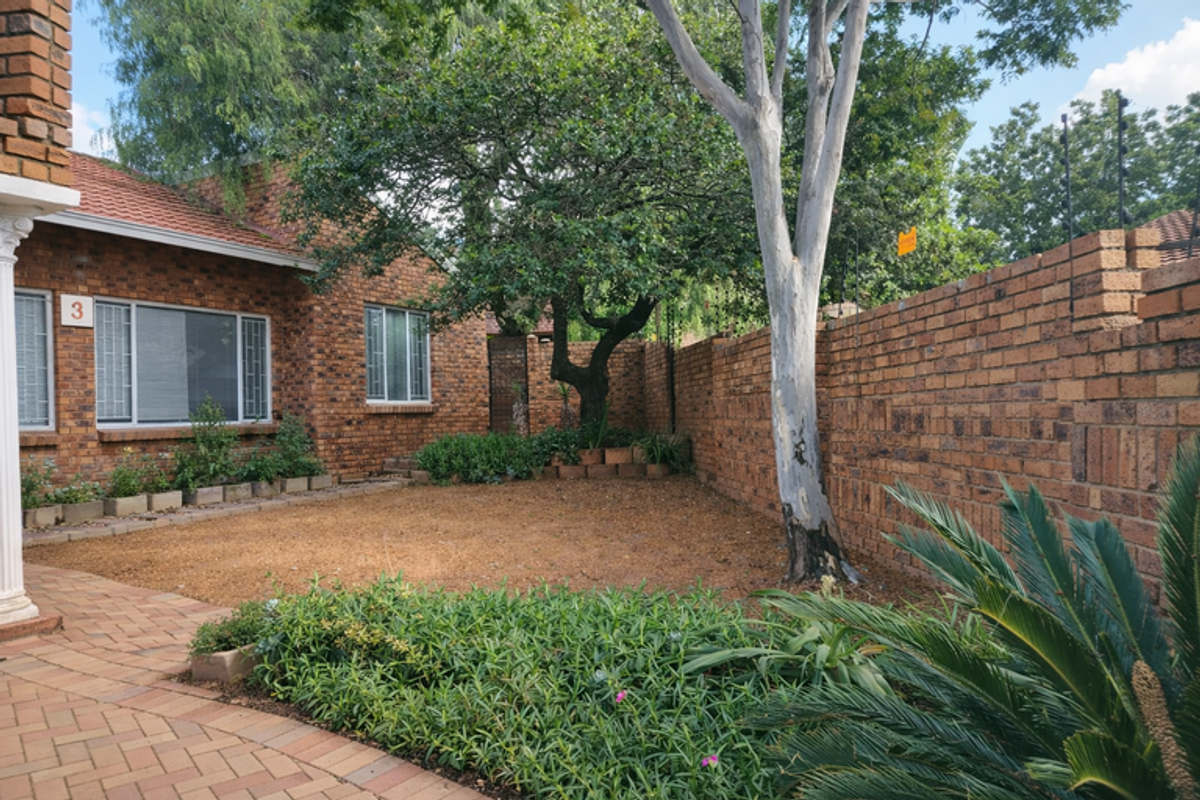 A private rear garden area featuring face brick walls, a paved walkway, and established landscaping with mature trees.