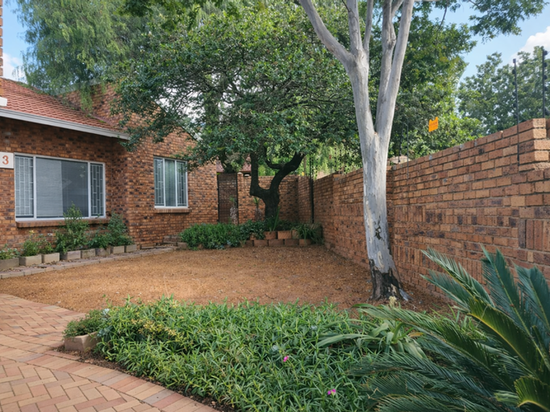 A private rear garden area featuring face brick walls, a paved walkway, and established landscaping with mature trees.