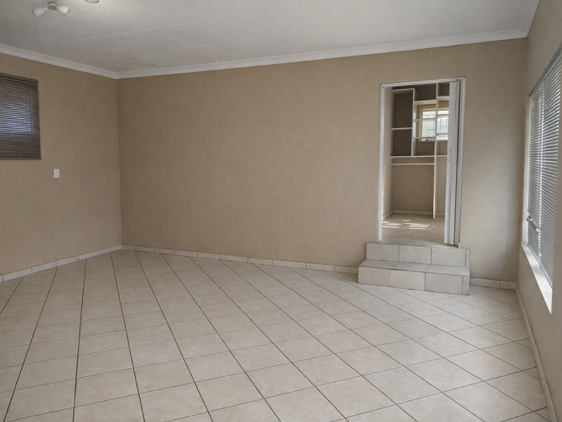 An empty living room featuring neutral tiled flooring, coved ceilings, and a small step leading to a built-in storage or utility area.