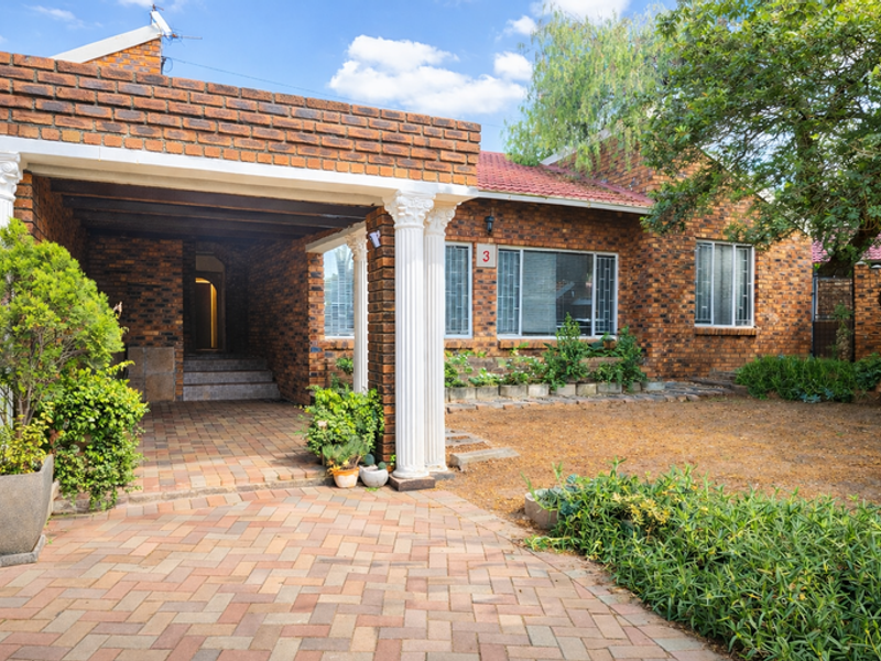 Front elevation of a face brick house featuring a covered patio with decorative columns and a paved entrance area.
