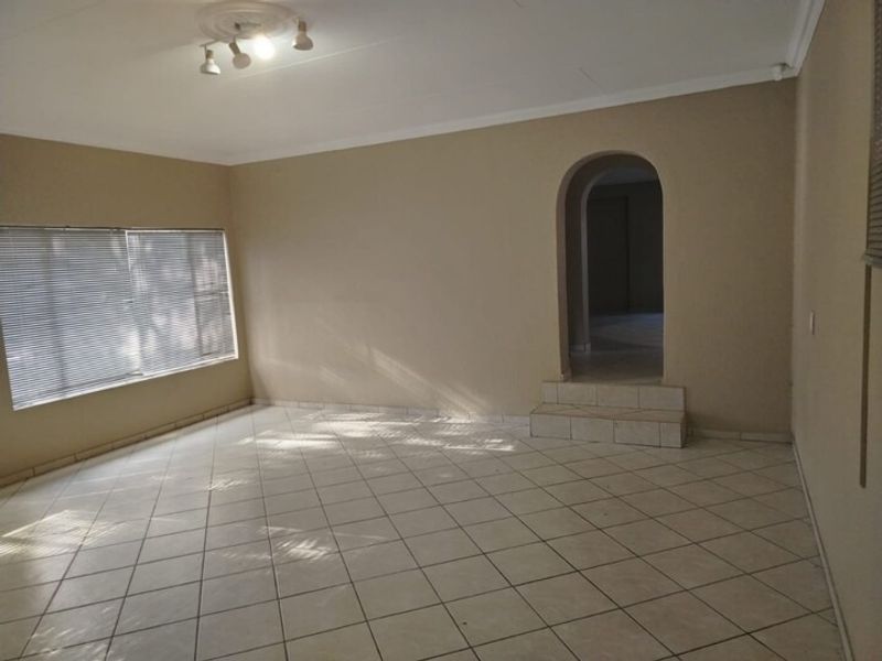 An empty living room featuring tiled flooring, an arched doorway with a tiled step, and natural light through venetian blinds.