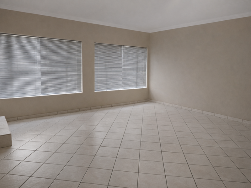 A spacious, empty living area featuring neutral wall tones, ceramic floor tiles, and large windows fitted with venetian blinds.