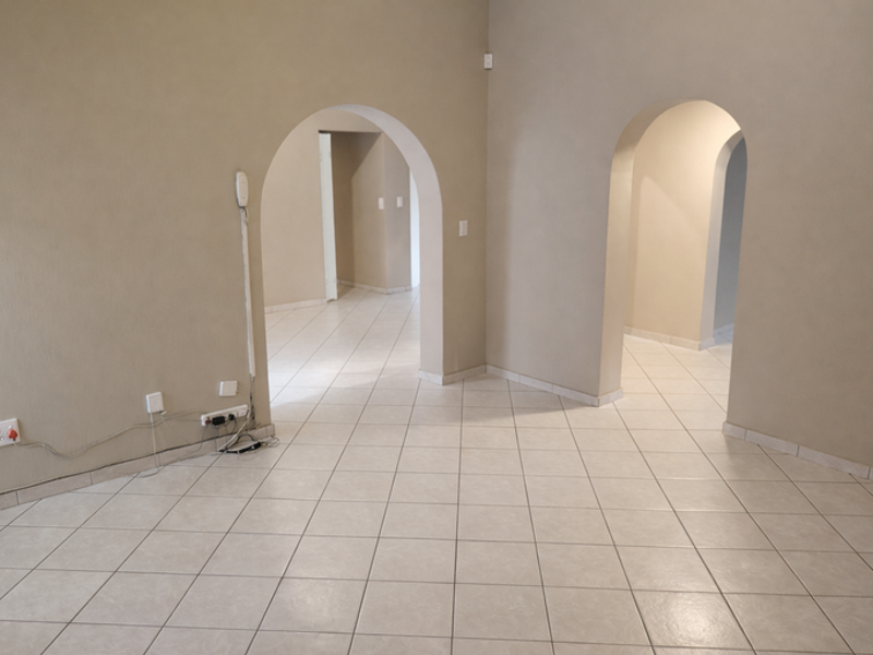 An empty living area featuring neutral tiled flooring and distinctive arched doorways leading to adjacent rooms, providing a versatile blank canvas.