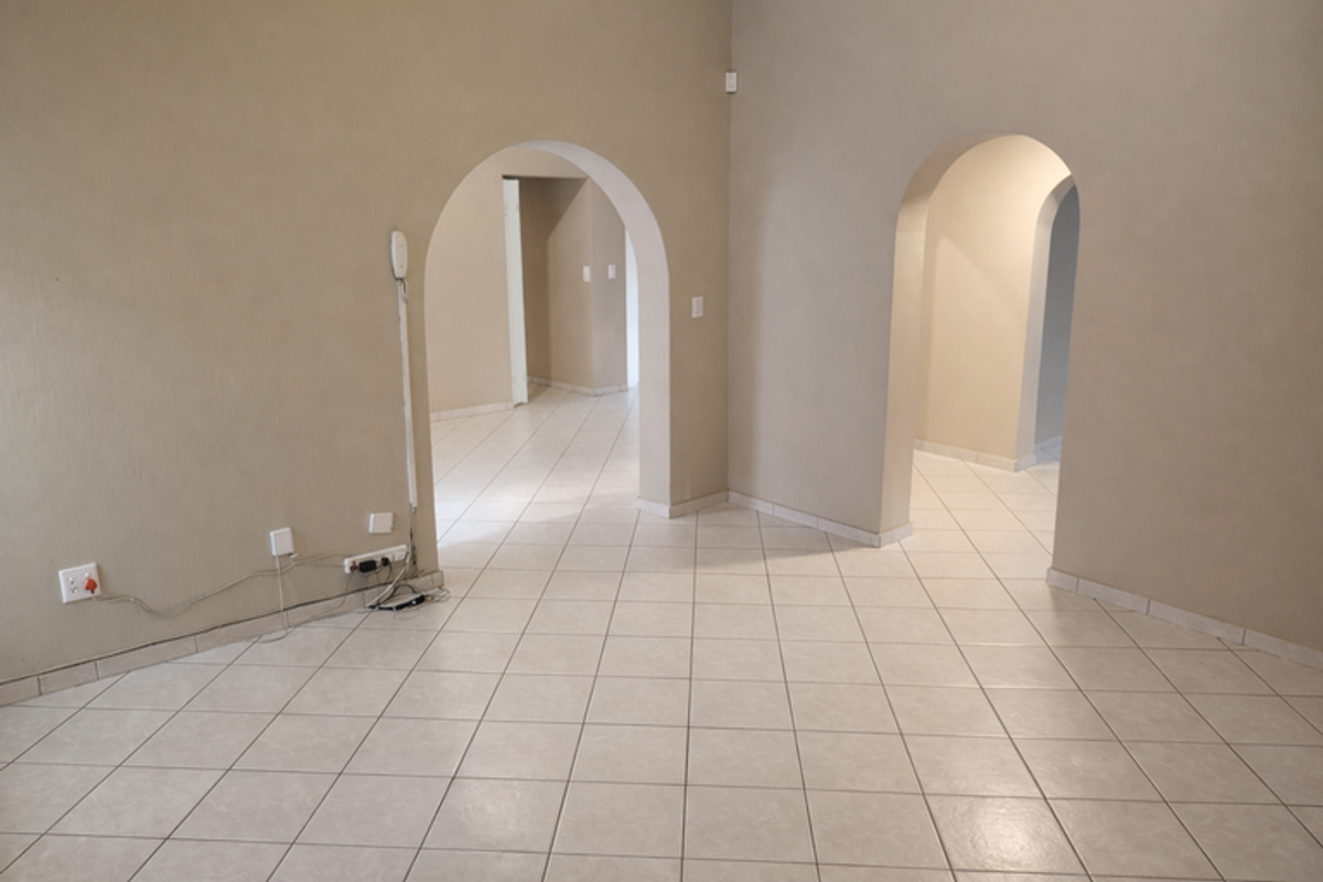 An empty living area featuring neutral tiled flooring and distinctive arched doorways leading to adjacent rooms, providing a versatile blank canvas.