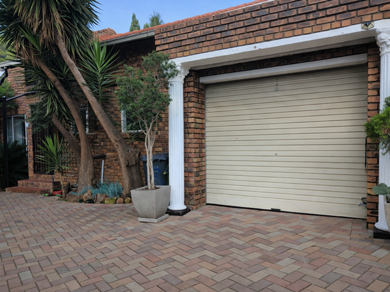 A brick-faced garage exterior featuring a secure roller shutter door, decorative columns, and a neatly paved driveway.