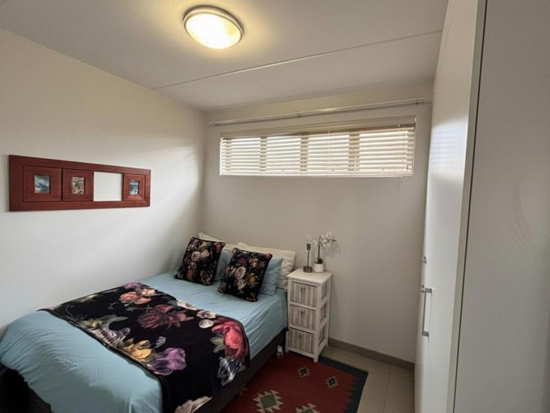 A compact bedroom featuring a built-in wardrobe, neutral wall finishes, and a window fitted with venetian blinds.