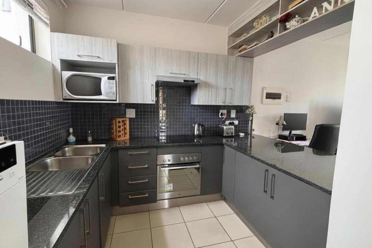 Modern kitchen featuring dark grey cabinetry, granite countertops, tiled backsplash, and integrated appliances, offering a functional and contemporary cooking space.