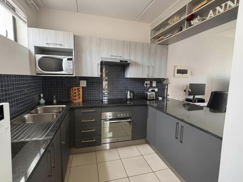 Modern kitchen featuring dark grey cabinetry, granite countertops, tiled backsplash, and integrated appliances, offering a functional and contemporary cooking space.