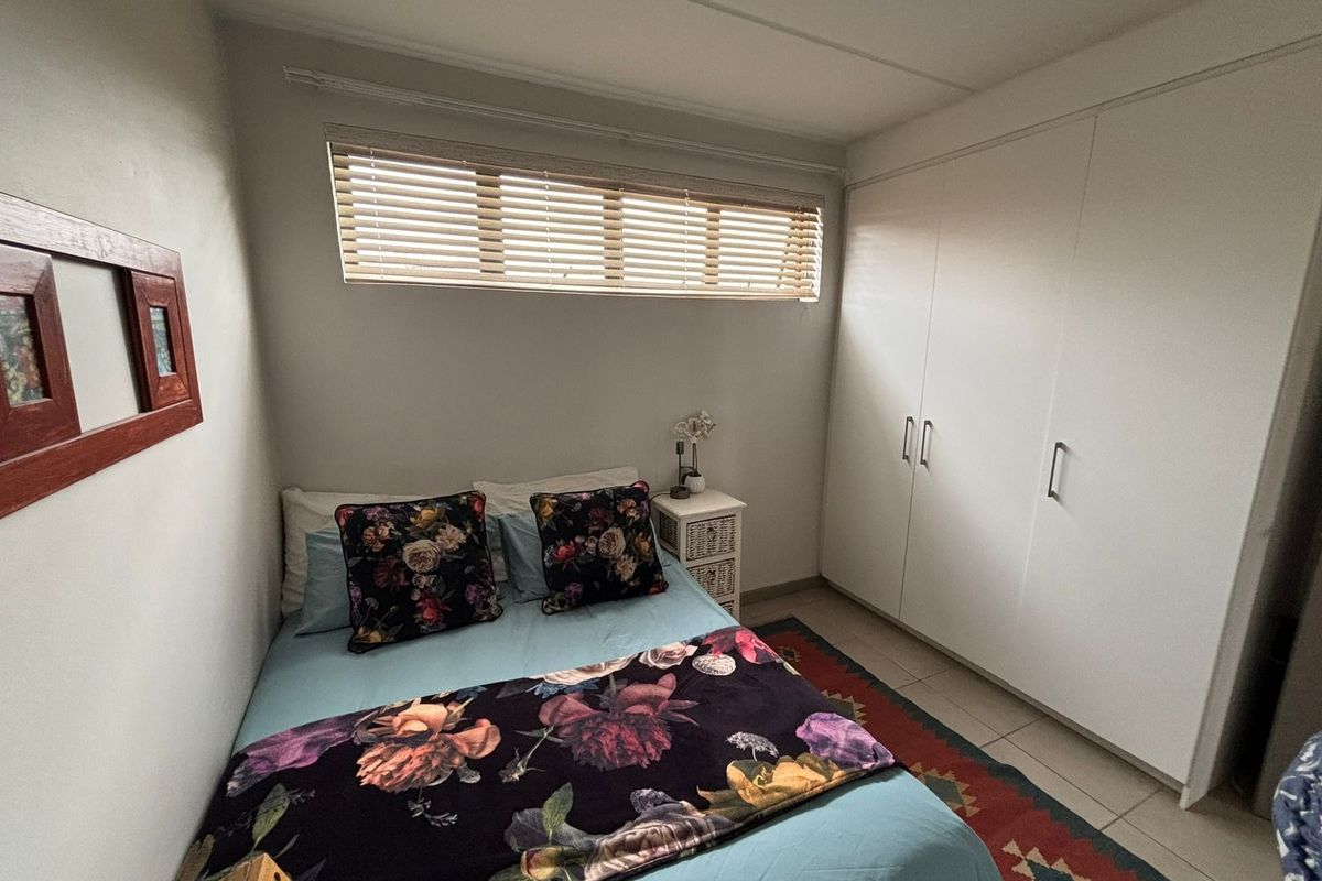A functional bedroom featuring built-in cupboards, tiled flooring, and a horizontal window with venetian blinds.