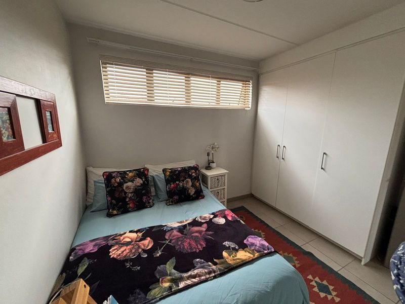 A functional bedroom featuring built-in cupboards, tiled flooring, and a horizontal window with venetian blinds.
