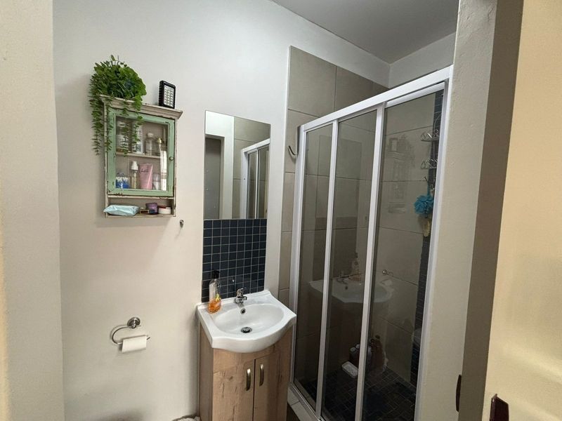 Compact bathroom featuring a vanity cabinet with basin, tiled splashback, and a glass-enclosed shower unit with neutral wall tiling.