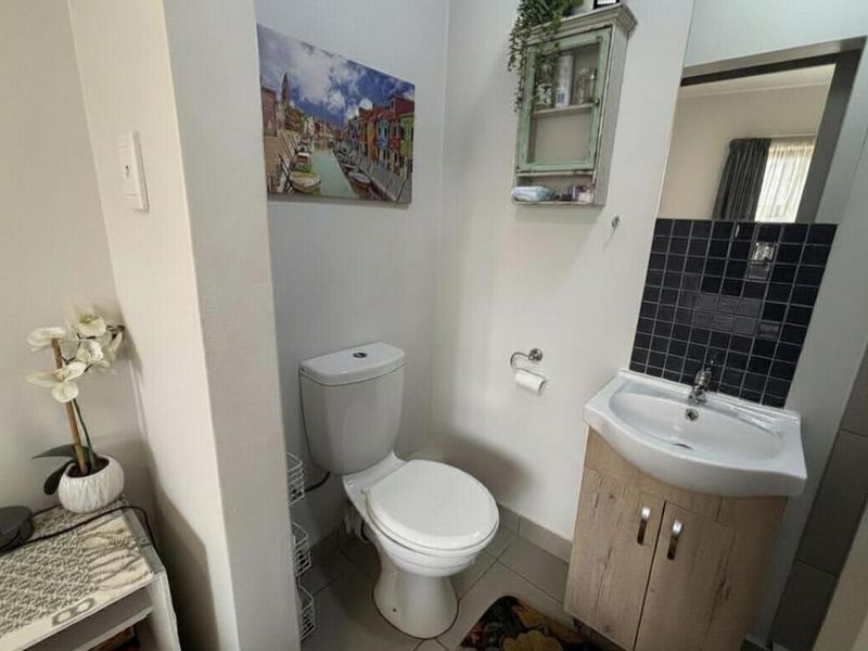 A compact bathroom featuring a white toilet, a vanity cabinet with a ceramic basin, and a black tiled splashback.