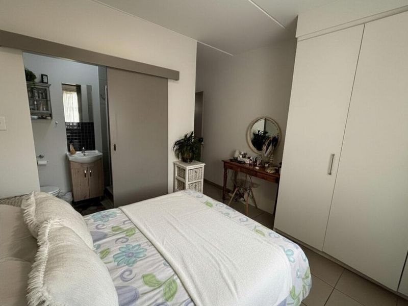 A well-maintained bedroom featuring built-in wardrobes, tiled flooring, and an adjoining en-suite bathroom with a vanity unit.