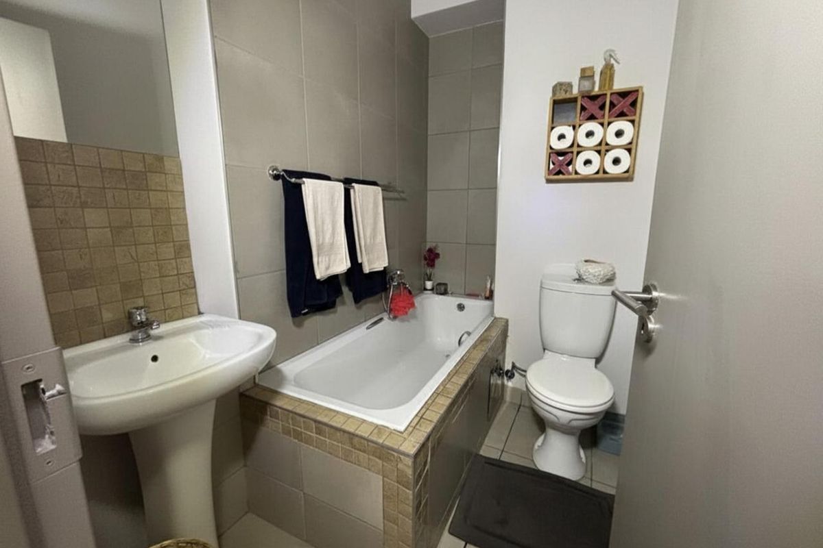 A functional bathroom featuring a pedestal basin, a built-in bathtub with tiled surround, and a standard toilet with neutral wall tiling.