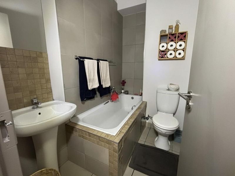 A functional bathroom featuring a pedestal basin, a built-in bathtub with tiled surround, and a standard toilet with neutral wall tiling.