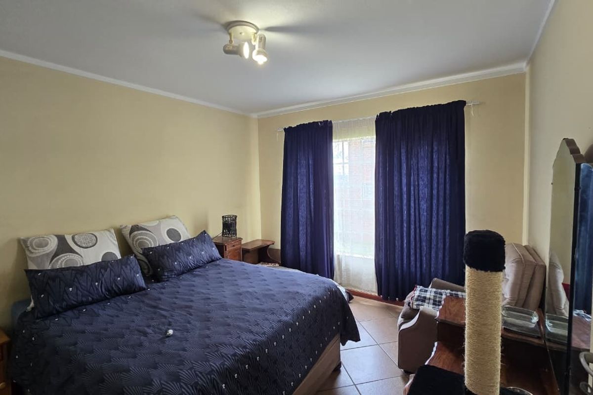 A standard bedroom featuring tiled flooring, a ceiling-mounted spotlight fixture, and a window fitted with security bars.