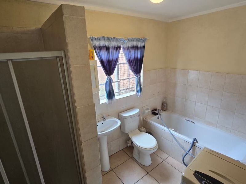 A functional bathroom featuring a shower enclosure, pedestal basin, toilet, and a built-in bathtub with partial wall tiling.
