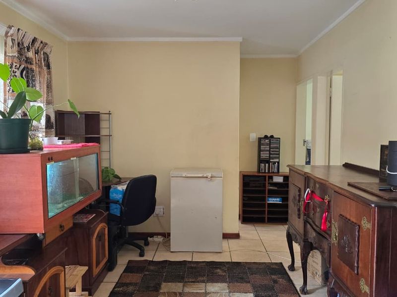 A living area featuring neutral wall paint and tiled flooring, providing a functional space with access to adjacent rooms.