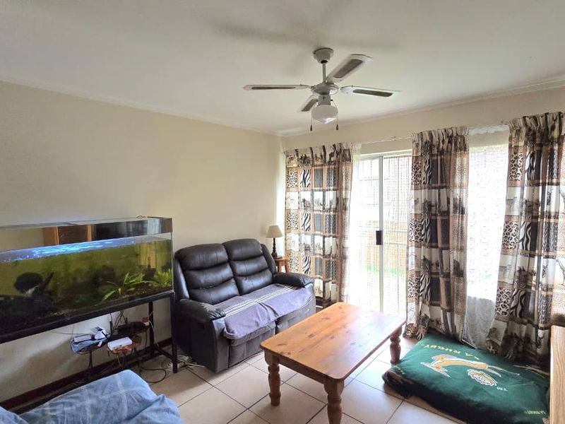 A living room featuring tiled flooring, a ceiling fan, and a sliding glass door providing access to the exterior.