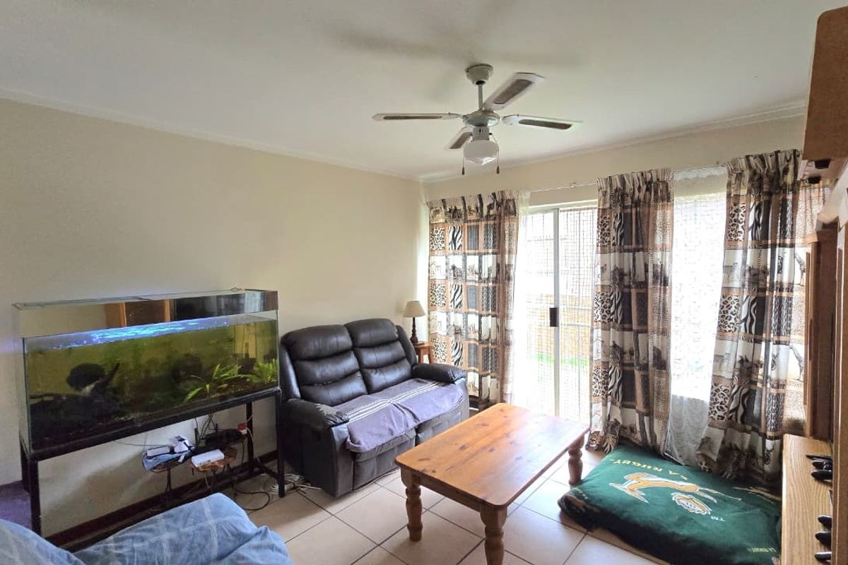 A living room featuring tiled flooring, a ceiling fan, and a sliding glass door providing access to the exterior.