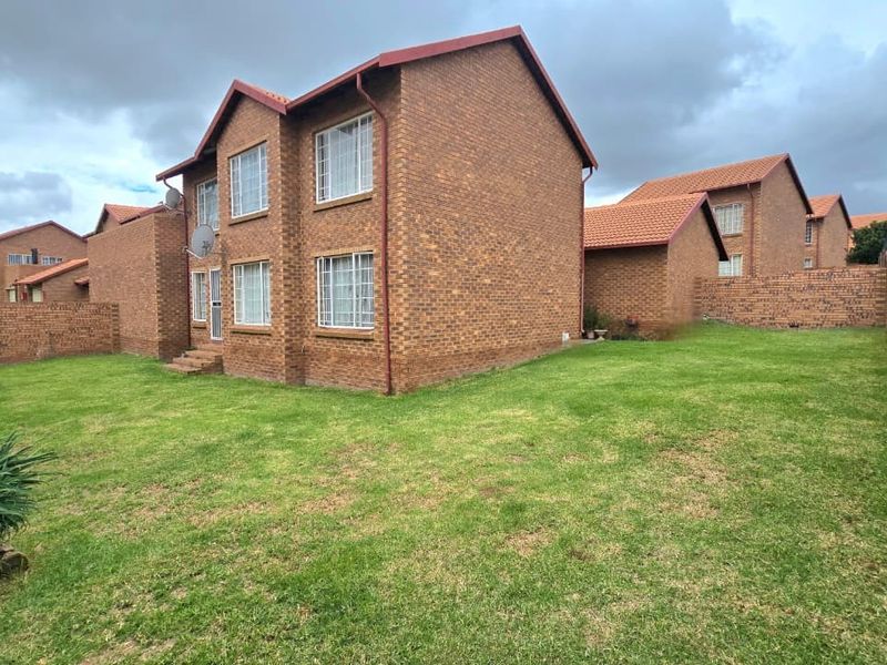Rear view of a face brick townhouse featuring a private garden, secure boundary walls with electric fencing, and tiled roofing.