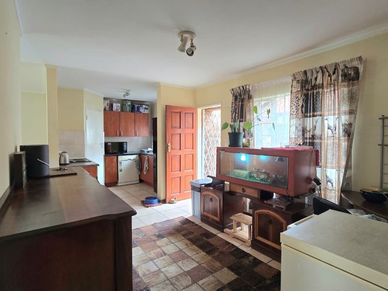 Open plan living and kitchen area featuring tiled flooring, wooden cabinetry, and direct access to the exterior via a security gate.