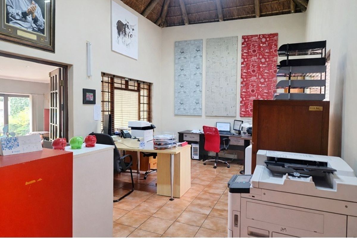 A functional home office space featuring high ceilings with exposed timber rafters, ceramic tiled flooring, and natural light through wooden-framed windows.
