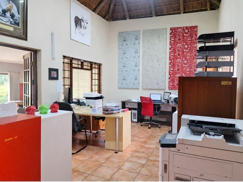 A functional home office space featuring high ceilings with exposed timber rafters, ceramic tiled flooring, and natural light through wooden-framed windows.