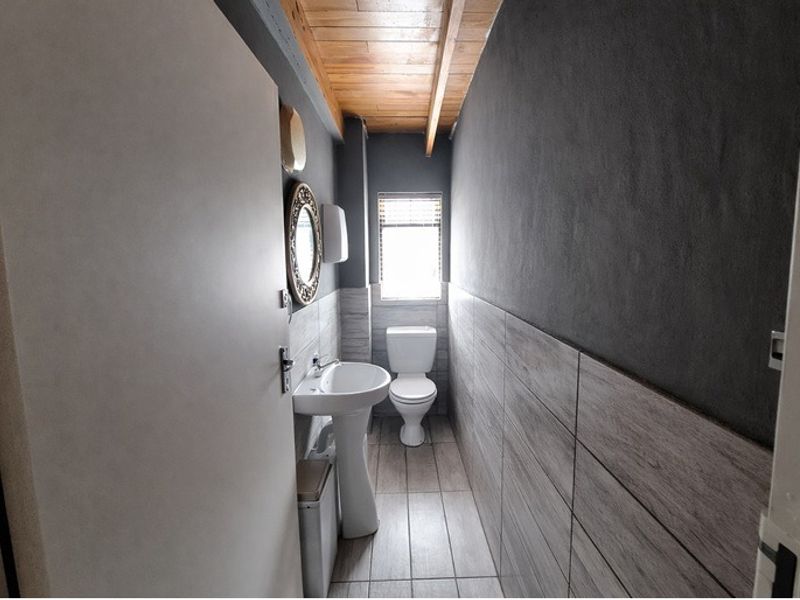 A compact bathroom featuring a pedestal sink, toilet, wood-paneled ceiling, and modern tiled finishes.