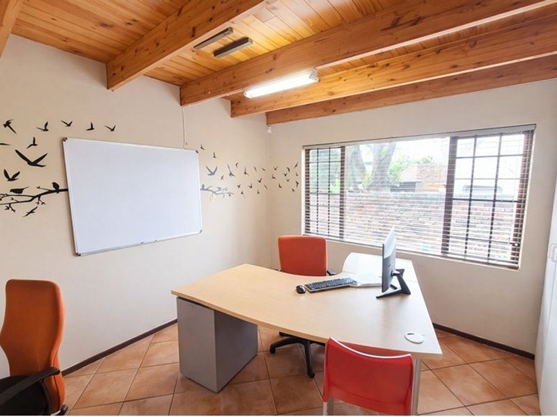 A functional home office featuring exposed timber beam ceilings, tiled flooring, and a built-in cupboard, providing a practical workspace with natural light.