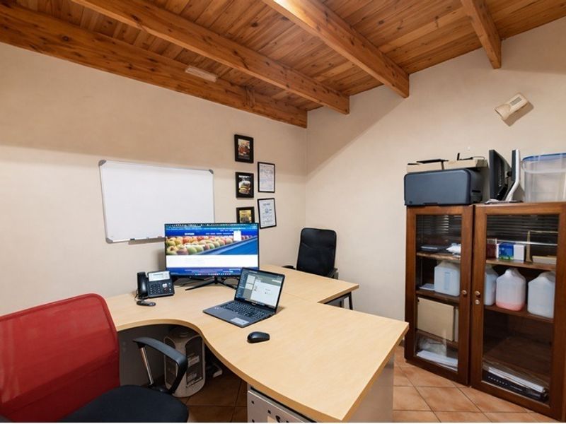 A functional home office featuring exposed timber beam ceilings and tiled flooring, providing a practical workspace environment.