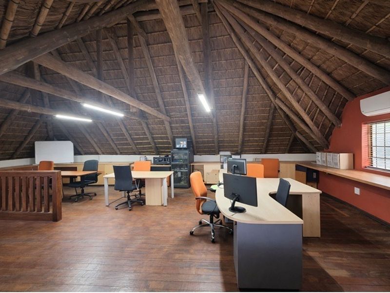 Spacious office area featuring a unique vaulted thatched ceiling with exposed timber trusses, timber flooring, and built-in desk space.