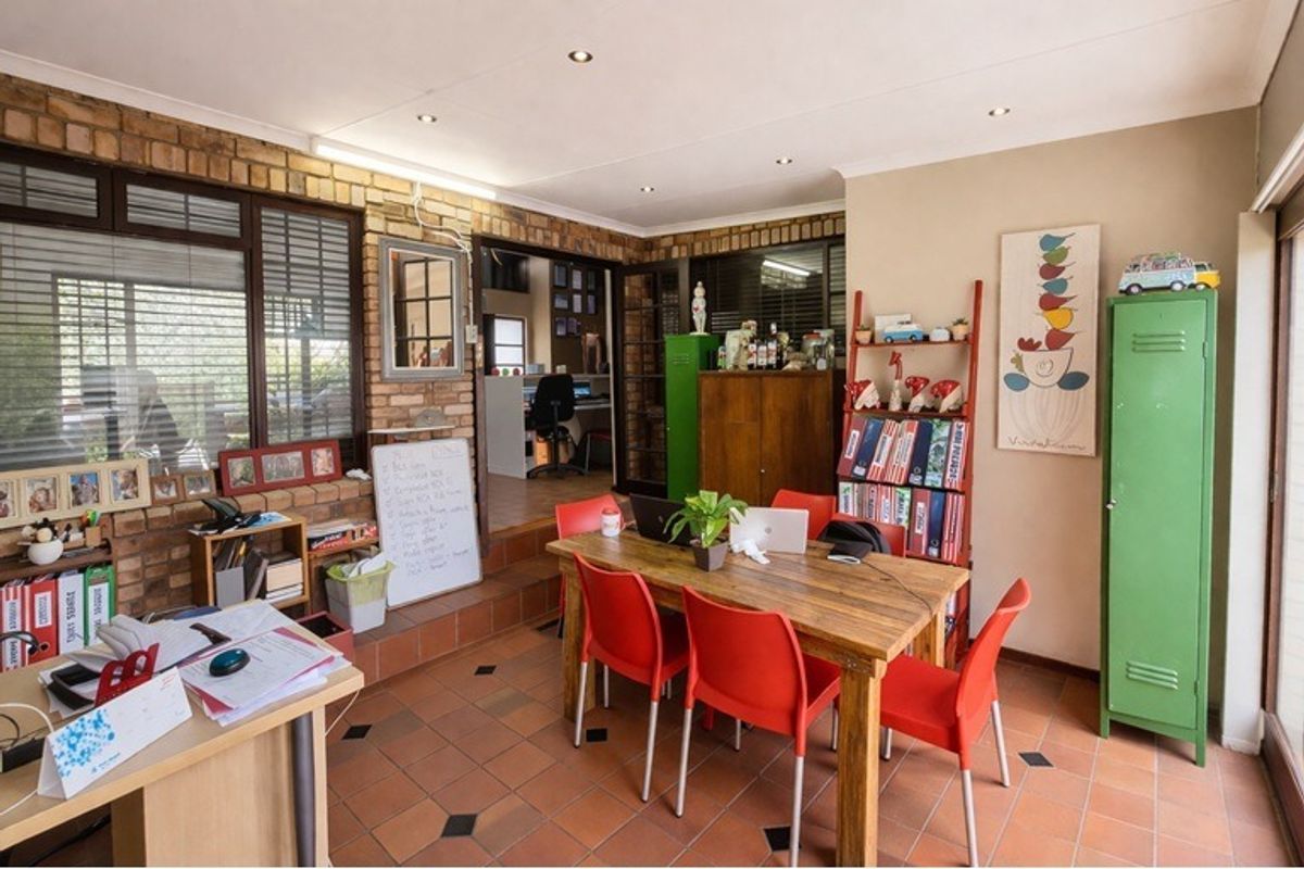 A multi-purpose living area featuring exposed brick walls, terracotta floor tiles, and recessed downlighting, offering a versatile space for dining or home office use.