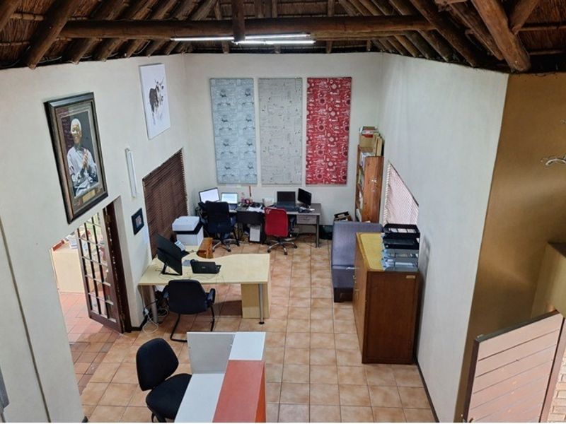 Spacious office area featuring high exposed thatch ceilings, ceramic tile flooring, and natural light, suitable for a professional workspace or home study.