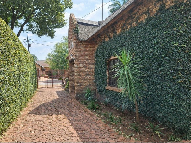 A charming brick-faced home with a traditional thatched roof, featuring a private cobblestone driveway and well-maintained perimeter hedging.