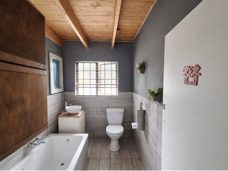 Modern bathroom featuring a vessel sink, built-in bathtub, and exposed timber ceiling beams with neutral wall and floor tiling.