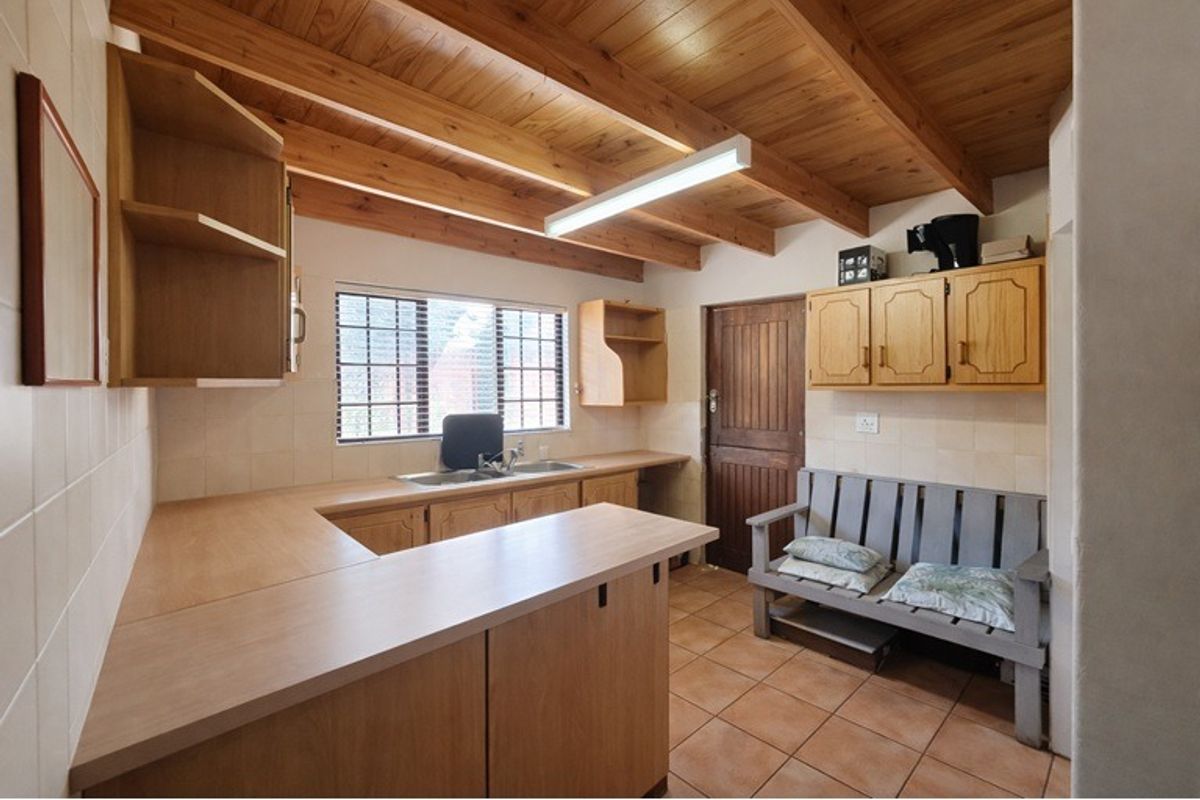 A functional kitchen featuring timber ceiling beams, laminate countertops, double basin sink, and ample built-in wooden cabinetry with tiled flooring.