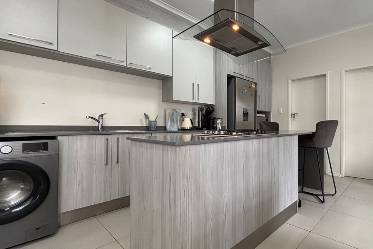Modern kitchen featuring light wood-grain cabinetry, stone countertops, a central island with a hob, and a stainless steel extractor fan.