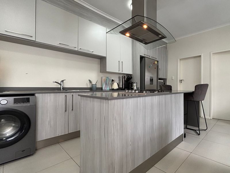 Modern kitchen featuring light wood-grain cabinetry, stone countertops, a central island with a hob, and a stainless steel extractor fan.